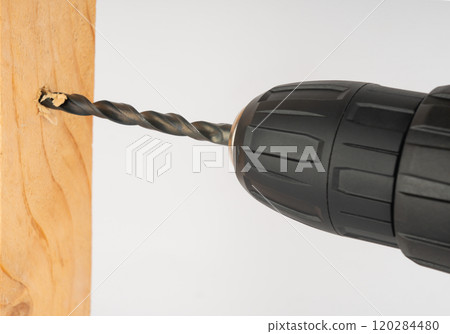 an electric drill drills a hole in a wooden board 120284480