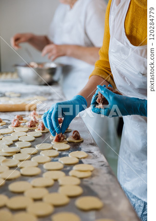 Making homemade dumplings, placing meat filling on dough circles in a busy kitchen environment Making homemade dumplings, placing meat filling on dough circles in a busy kitchen environment 120284779