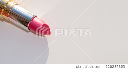 Close-up of a part of a golden tube of lipstick on a white background with a copy of the space on the right 120286863