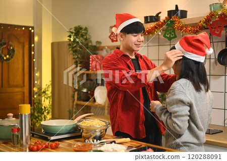 Cheerful young couple enjoying Christmas preparations together in a decorated kitchen Cheerful young couple enjoying Christmas preparations together in a decorated kitchen 120288091