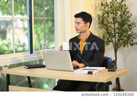 Handsome businessman taking a break and enjoying a coffee at desk Handsome businessman taking a break and enjoying a coffee at desk 120288160