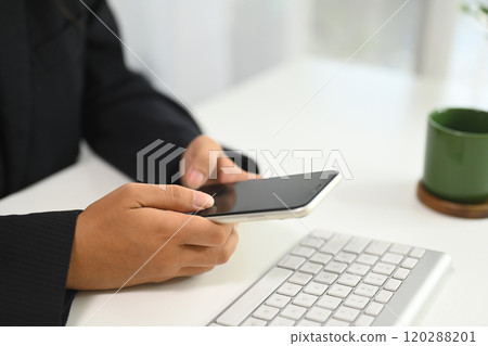 Close up of businesswoman using mobile phone next to computer keyboard at office desk Close up of businesswoman using mobile phone next to computer keyboard at office desk 120288201
