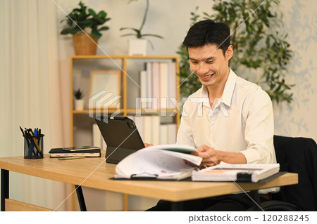 Smiling adult businessman analyzing financial reports and using digital tablet at desk Smiling adult businessman analyzing financial reports and using digital tablet at desk 120288245