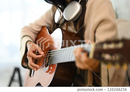 Close up of woman playing acoustic guitar with headphones around neck 120288256