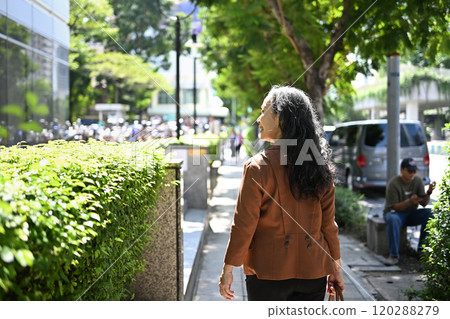 Back view of confident senior businesswoman strolling through urban greenery 120288279