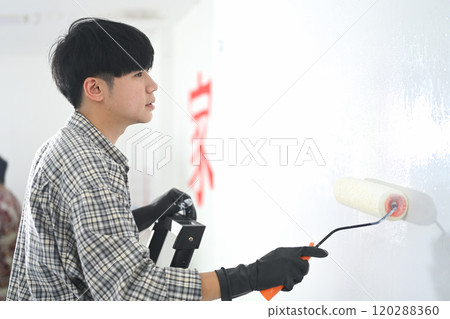 Young asian man painting a wall with roller brush during renovation 120288360