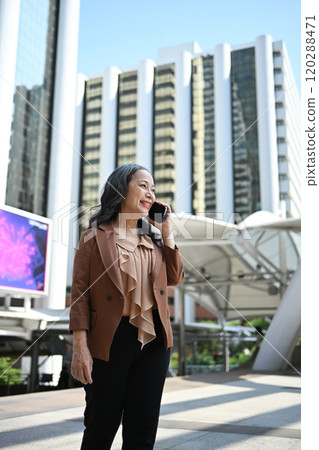 Portrait of elegant mature entrepreneur talking on mobile phone with skyscrapers in the background Portrait of elegant mature entrepreneur talking on mobile phone with skyscrapers in the background 120288471