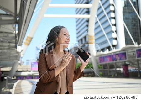 Beautiful mature businesswoman holding smartphone standing outside modern office building Beautiful mature businesswoman holding smartphone standing outside modern office building 120288485
