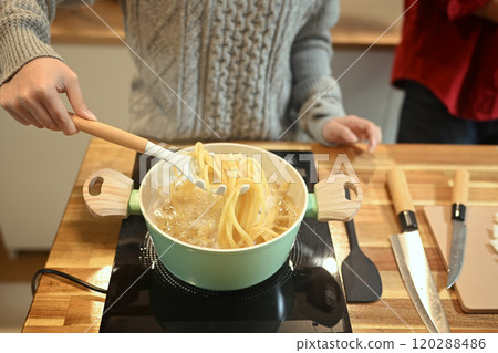 Young couple cooking pasta in a green pot on a stove during the festive season 120288486