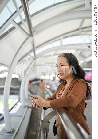 Smiling mature woman using smartphone in a busy urban space Smiling mature woman using smartphone in a busy urban space 120288487