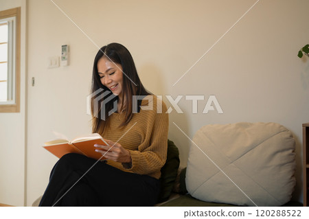 Relaxed young woman in brown sweater reading a book on sofa at home Relaxed young woman in brown sweater reading a book on sofa at home 120288522