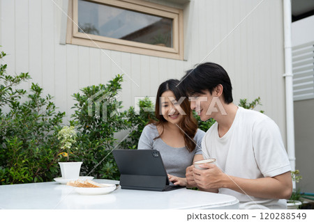 Happy young Asian couple using digital tablet and spending time together in backyard Happy young Asian couple using digital tablet and spending time together in backyard 120288549