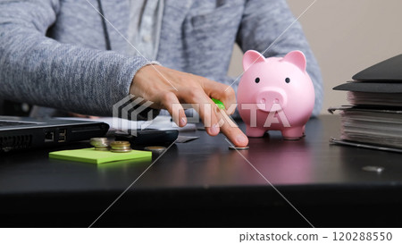 Man empties a pink piggy bank filled with coins in the office, taking notes while managing his finances Man empties a pink piggy bank filled with coins in the office, taking notes while managing his finances 120288550
