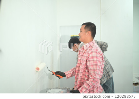 Young man painting a wall using a paint roller in newly renovated space. Home Improvement concept 120288573