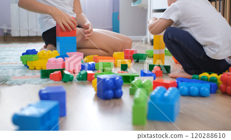 A young girl and her baby sister joyfully build towers with colorful toy blocks in their cozy nursery, enjoying playtime together 120288610