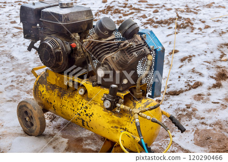 Portable air compressor sits in mud on construction site, with dirt scattered around equipment indicating active work. Portable air compressor sits in mud on construction site, with dirt scattered around equipment indicating active work. 120290466