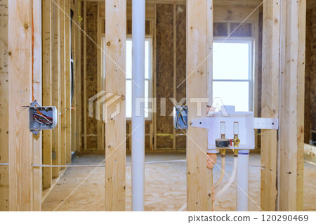 Construction of new home interior featuring exposed wooden frame, plumbing connecting laundry systems, electrical wiring during renovation 120290469