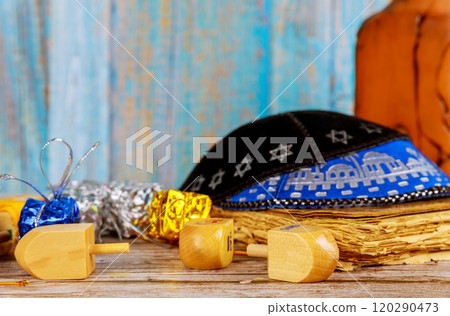 Colorful dreidels chocolate gelt rest on wooden table, accompanied by traditional kippah, creating festive atmosphere for Hanukkah celebrations. 120290473