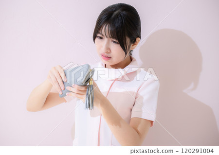 A female nurse is troubled because she is short of money and is looking at her wallet Pink background A female nurse is troubled because she is short of money and is looking at her wallet Pink background 120291004