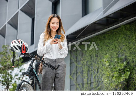 On a city bike ride a cheerful woman stays connected with her smartphone. Her happy expression embodies the modern concept of balancing work and leisure through technology. On a city bike ride a cheerful woman stays connected with her smartphone. Her happy expression embodies the modern concept of balancing work and leisure through technology. 120293469