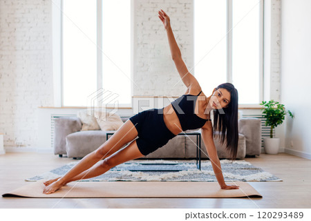 Woman standing in side plank exercise practicing yoga Vasisthasana pose, working out at home, wearing sportswear, full length Woman standing in side plank exercise practicing yoga Vasisthasana pose, working out at home, wearing sportswear, full length 120293489