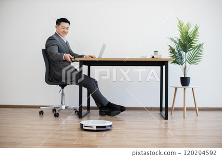 Asian businessman working at desk with robot vacuum cleaning Asian businessman working at desk with robot vacuum cleaning 120294592