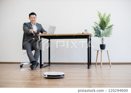 Asian businessman working with laptop and robot vacuum in office 120294600