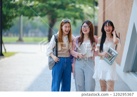 Three young women are walking down a sidewalk, smiling and holding books Three young women are walking down a sidewalk, smiling and holding books 120295367