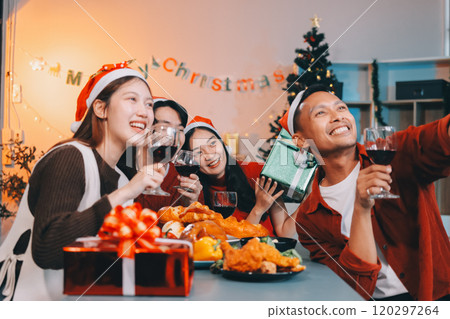 Group of young Asian man and women as friends having fun at a New Year's celebration, holding gift boxes standing by Christmas tree decoration, midnight countdown Party at home with holiday season. 120297264
