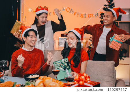 Group of young Asian man and women as friends having fun at a New Year's celebration, holding gift boxes standing by Christmas tree decoration, midnight countdown Party at home with holiday season. 120297337