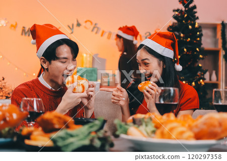 Group of young Asian man and women as friends having fun at a New Year's celebration, holding gift boxes standing by Christmas tree decoration, midnight countdown Party at home with holiday season. 120297358