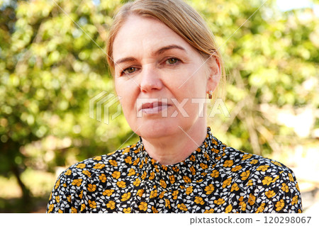 A woman in her 40s with blonde hair, walking through nature. Her face reflects a sense of calm and enjoyment as she takes a leisurely walk 120298067