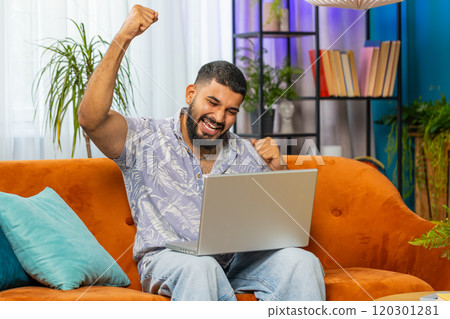 Amazed Indian man use laptop computer, receive good news message, shocked by victory, celebrate win 120301281