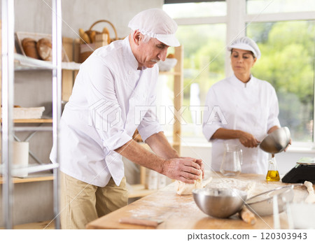 Elderly male chef and female skillfully kneads dough to bake delicious bread and croissants Elderly male chef and female skillfully kneads dough to bake delicious bread and croissants 120303943