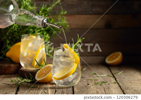 Cocktail gin tonic with ice, lemon, and rosemary on a old wooden table. Cocktail gin tonic with ice, lemon, and rosemary on a old wooden table. 120306279