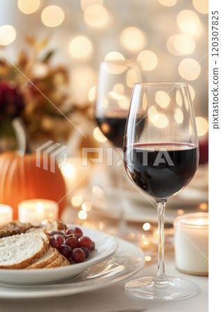 Elegant dining setup with wine glasses, bread, and seasonal decorations in cozy ambient lighting 120307825