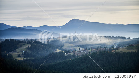Misty mountain landscape at dawn, with layers of dark green forests and rolling hills. Small rural homes and communication tower scattered across hillsides. Distant mountains bathed in soft light. Misty mountain landscape at dawn, with layers of dark green forests and rolling hills. Small rural homes and communication tower scattered across hillsides. Distant mountains bathed in soft light. 120307987