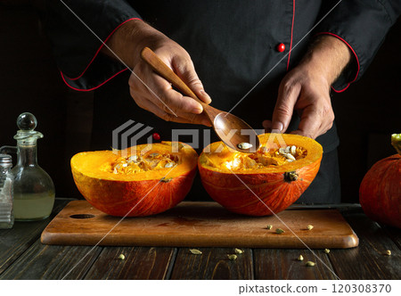 A chef carefully scoops out seeds from a halved pumpkin in a cozy kitchen. The warm colors and wooden textures evoke a perfect autumn ambiance, highlighting seasonal cooking A chef carefully scoops out seeds from a halved pumpkin in a cozy kitchen. The warm colors and wooden textures evoke a perfect autumn ambiance, highlighting seasonal cooking 120308370