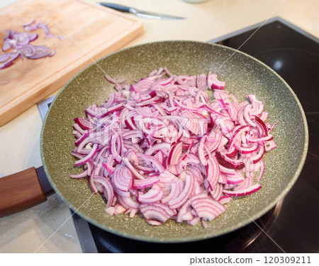 Slicing red onions in a frying pan on a kitchen countertop during meal preparation Slicing red onions in a frying pan on a kitchen countertop during meal preparation 120309211