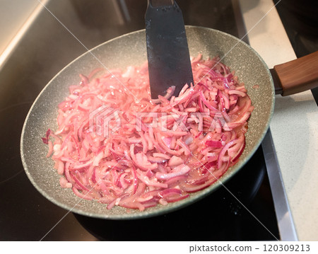 Sauting sliced red onions in a frying pan on a stovetop for a flavorful meal 120309213