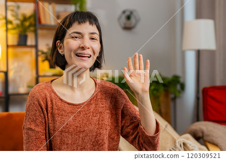 Caucasian woman smiling friendly at camera and waving hands gesturing hello hi greeting at home 120309521