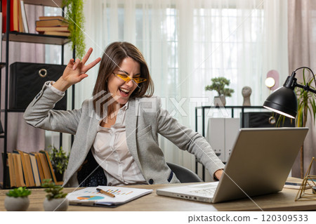 Happy business woman working on laptop at home office desk putting on earbuds listening music relax Happy business woman working on laptop at home office desk putting on earbuds listening music relax 120309533