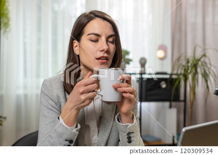 Businesswoman drinking cup of warm hot coffee sitting at table office workplace relax taking a break 120309534