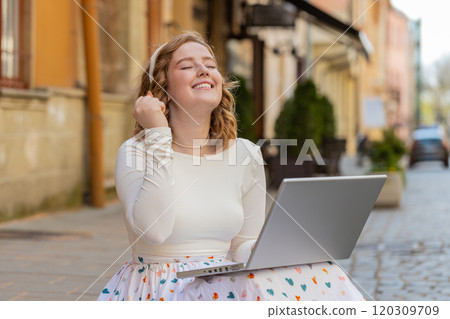 Caucasian happy woman working on laptop celebrate success win money sitting on urban street in city 120309709