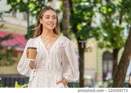 Happy smiling woman walking on city street enjoying morning coffee hot drink relaxing taking a break 120309773