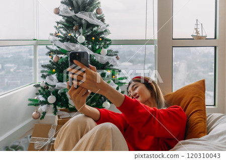 Happy red shirt woman making a video call holiday greeting with her friends and family showing the Christmas tree. Happy red shirt woman making a video call holiday greeting with her friends and family showing the Christmas tree. 120310043