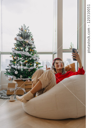 Happy red shirt woman making a video call holiday greeting with her friends and family showing the Christmas tree. Happy red shirt woman making a video call holiday greeting with her friends and family showing the Christmas tree. 120310051