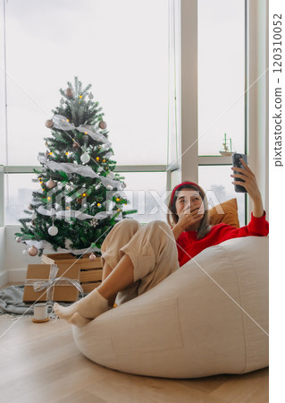 Happy red shirt woman making a video call holiday greeting with her friends and family showing the Christmas tree. Happy red shirt woman making a video call holiday greeting with her friends and family showing the Christmas tree. 120310052