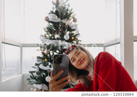 Happy red shirt woman making a video call holiday greeting with her friends and family showing the Christmas tree.  120310064