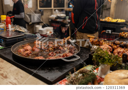 Grilled sausages, pork in street market in a medieval fair. Sausages and pork ready to eat. Festival of street food and meat. Selling traditional hot food at the Christmas Fair. Chief cooking meat 120311369